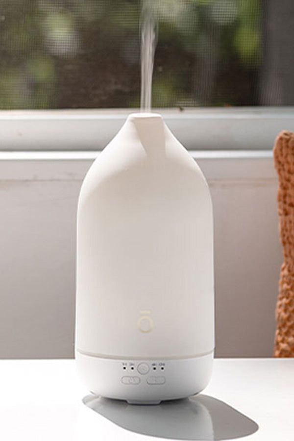 A white essential oil diffuser with misting at the top, sitting on a white surface in front of a window. dōTERRA Laluz Diffuser with Lemon and Lavender