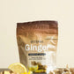 A stand-up pouch of doTERRA Ginger Digestive Drops displayed on a wooden surface with ginger root slices, lemon wedges, and wrapped capsules around it, against a plain beige background. doTERRA Ginger Digestive Drops (2 Pack)