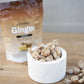 A stand-up pouch of DoTERRA Ginger candy sits on a wooden tabletop behind a small white marble bowl filled with ginger candies, with a few candies scattered nearby.