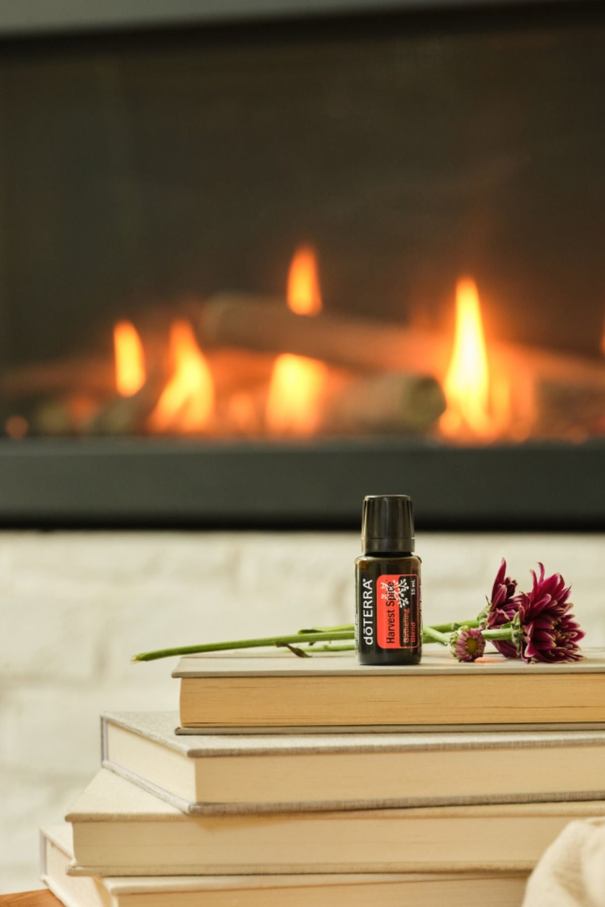 A small bottle of doTERRA cat spray placed on a stack of books in front of a warm fireplace, with a flower resting beside it. dōTERRA Harvest Spice Blend | Canada