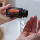A person holds an open bottle of doTERRA On Guard+ Protective Blend Softgels over their palm, with a small amber softgel visible in their other hand, set against a softly blurred bathroom background. doTERRA On Guard Softgels (2 Pack)