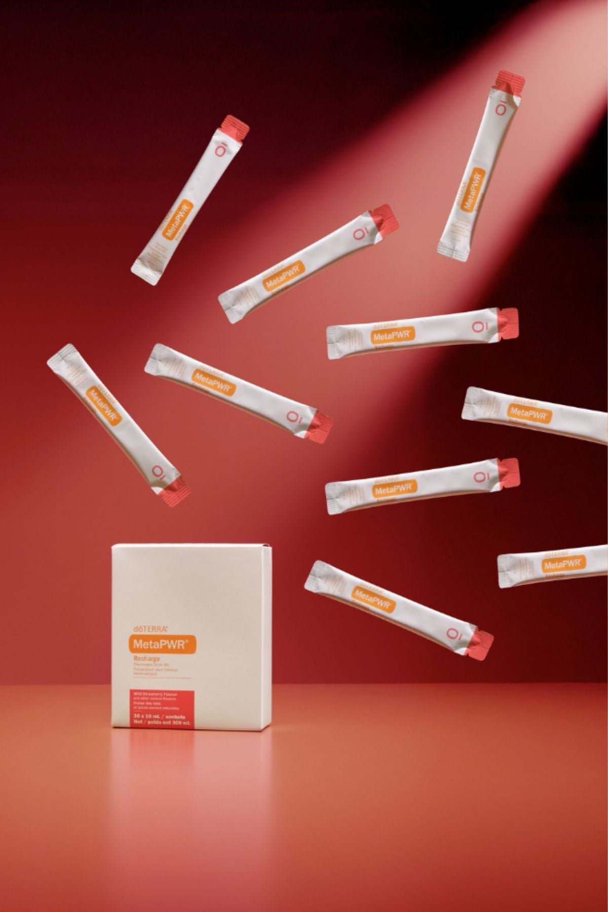 A white rectangular box labeled MegaPWT stands on a red surface, with multiple white single-serve packets floating around it against a red studio background. dōTERRA MetaPWR Recharge Electrolytes (Wild Strawberry)