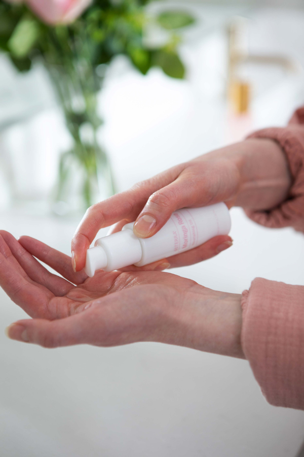 Person applying a white bottle of lotion to their hand with a blurred background