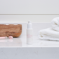 Cosmetic bottle on a bathroom counter with a towel and wooden cutting board in the background