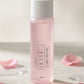 A bottle of IKISE 3 | Lotion - Smooth & Soft in a translucent light pink bottle with a white cap, styled on a light beige surface with scattered pink rose petals.
